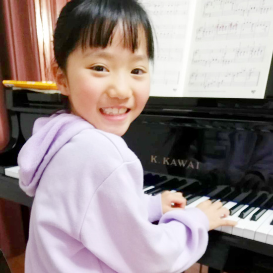 ピアノを弾きながら振り返る女の子の生徒写真