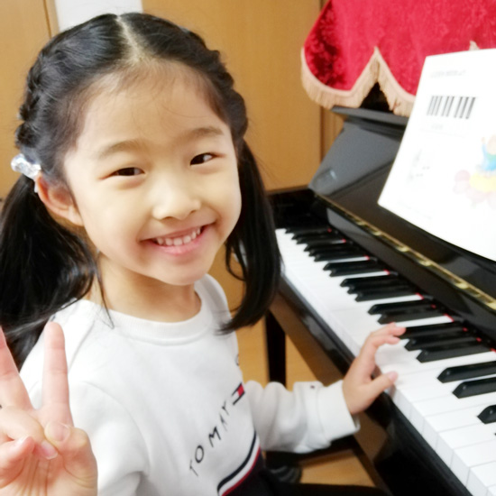 ピアノの前でピースする女の子の生徒写真