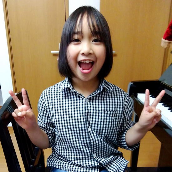 ピアノの前でピースする女の子の生徒写真